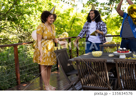 Friends celebrating outdoors with party hats, enjoying snacks and laughter on deck 135634576