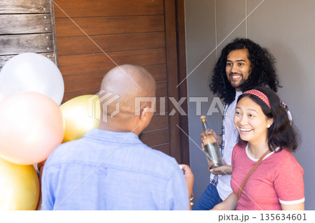 Friends arriving at party with balloons and bottle, smiling and excited Friends arriving at party with balloons and bottle, smiling and excited 135634601