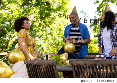 Friends celebrating birthday outdoors with balloons and party hats, sharing laughter Friends celebrating birthday outdoors with balloons and party hats, sharing laughter 135634602