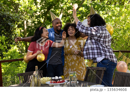 Celebrating outdoors, friends wearing party hats with balloons at festive gathering 135634608