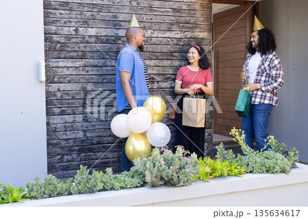 Friends celebrating with balloons and gifts, smiling and chatting at front porch Friends celebrating with balloons and gifts, smiling and chatting at front porch 135634617