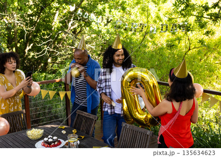 Celebrating birthday outdoors, friends decorating with balloons and wearing party hats Celebrating birthday outdoors, friends decorating with balloons and wearing party hats 135634623