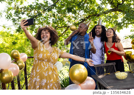 Friends celebrating outdoors, taking selfie with party hats and balloons 135634628
