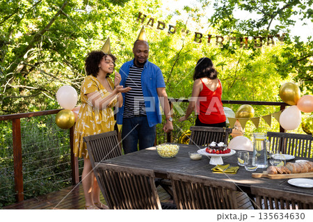 Wearing party hats, friends celebrating birthday outdoors with festive decorations Wearing party hats, friends celebrating birthday outdoors with festive decorations 135634630