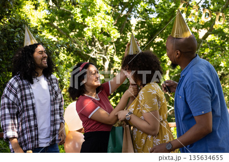 Celebrating outdoors, friends wearing party hats, laughing in festive atmosphere Celebrating outdoors, friends wearing party hats, laughing in festive atmosphere 135634655