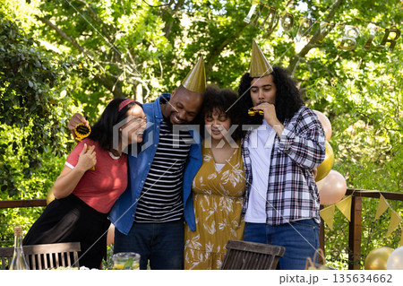 Celebrating outdoors, friends wearing party hats and smiling in festive atmosphere 135634662