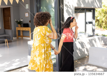 Two women holding hands and laughing together outside modern home Two women holding hands and laughing together outside modern home 135634667