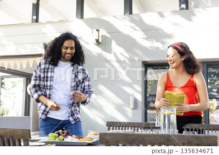 Friends preparing outdoor table with food and drinks, smiling and enjoying together Friends preparing outdoor table with food and drinks, smiling and enjoying together 135634671