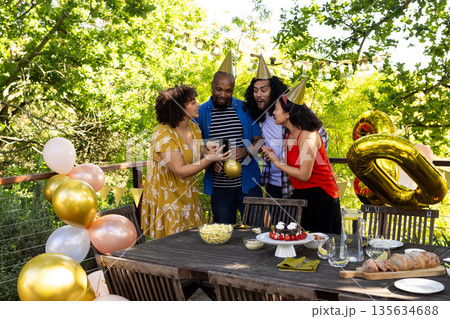 Friends celebrating birthday outdoors, wearing party hats and sharing joyful moments Friends celebrating birthday outdoors, wearing party hats and sharing joyful moments 135634688