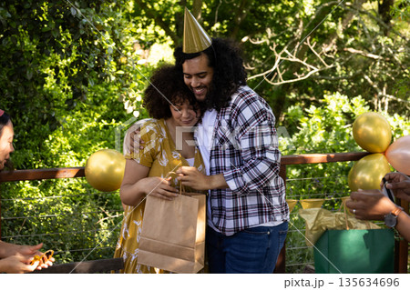 Celebrating outdoors, couple hugging and exchanging gifts at festive party Celebrating outdoors, couple hugging and exchanging gifts at festive party 135634696