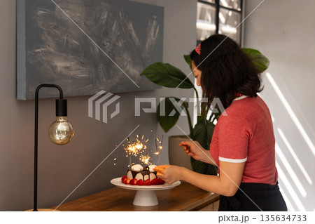 Woman decorating cake with sparklers at home, preparing for celebration 135634733