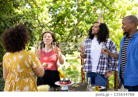 Friends celebrating outdoors with champagne, wearing party hats, enjoying sunny day Friends celebrating outdoors with champagne, wearing party hats, enjoying sunny day 135634766