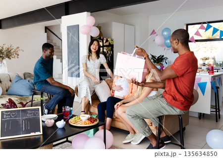 Friends celebrating baby shower at home, giving gifts and enjoying snacks together Friends celebrating baby shower at home, giving gifts and enjoying snacks together 135634850