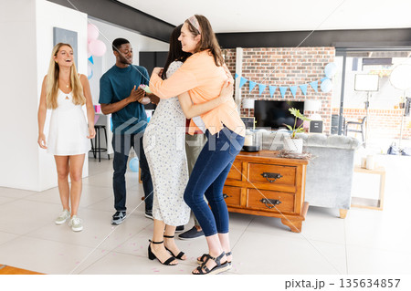 Friends celebrating at home, hugging and laughing during joyful gathering 135634857