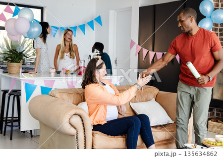 African American man handing gift to pregnant woman at home baby shower celebration African American man handing gift to pregnant woman at home baby shower celebration 135634862