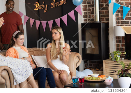 Friends enjoying baby shower party, chatting and eating snacks in cozy living room Friends enjoying baby shower party, chatting and eating snacks in cozy living room 135634864