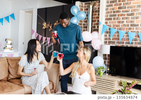 Friends celebrating baby shower at home, raising glasses with joyful smiles 135634874