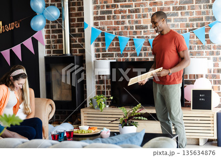 African American man holding gift at home during gender reveal party, smiling warmly African American man holding gift at home during gender reveal party, smiling warmly 135634876