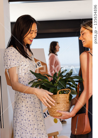 Friends exchanging potted plant gift at home, smiling and enjoying celebration Friends exchanging potted plant gift at home, smiling and enjoying celebration 135634896