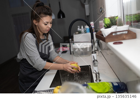 Woman Washes Lemon in Kitchen Sink During Evening Hours 135635146