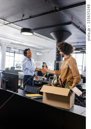 Colleagues shaking hands in modern office, welcoming new team member with box Colleagues shaking hands in modern office, welcoming new team member with box 135635248
