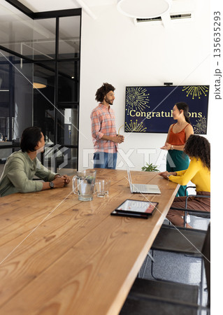 Celebrating success, team discussing achievements with congratulatory screen in office 135635293