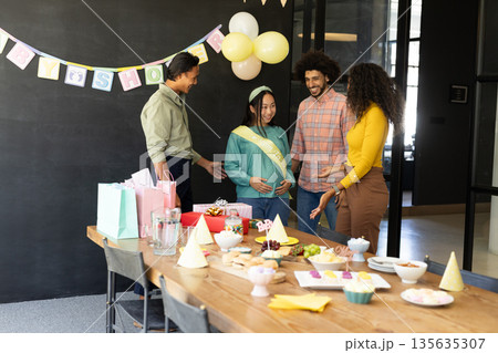 Celebrating baby shower, diverse friends congratulating expectant mother in office setting Celebrating baby shower, diverse friends congratulating expectant mother in office setting 135635307