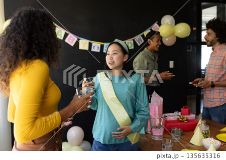 Expectant mother celebrating baby shower with friends, sharing conversation and laughter Expectant mother celebrating baby shower with friends, sharing conversation and laughter 135635316