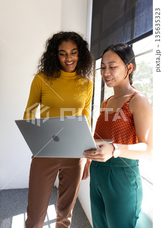 Two women collaborating on laptop in office, sharing ideas and smiling Two women collaborating on laptop in office, sharing ideas and smiling 135635323
