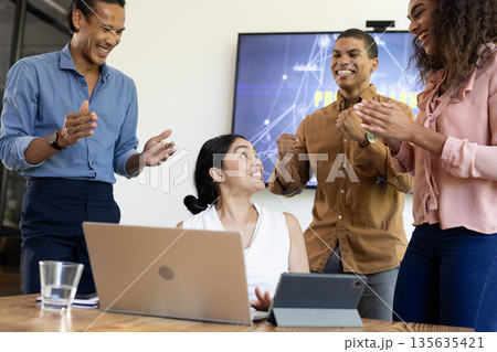 Diverse business team celebrating success with laptop and tablet in modern office Diverse business team celebrating success with laptop and tablet in modern office 135635421