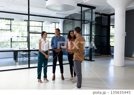 Diverse business team discussing project in modern office, standing and smiling Diverse business team discussing project in modern office, standing and smiling 135635445