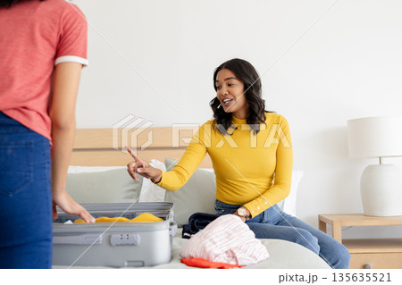 Mother in yellow sweater packing suitcase with daughter, preparing for travel Mother in yellow sweater packing suitcase with daughter, preparing for travel 135635521