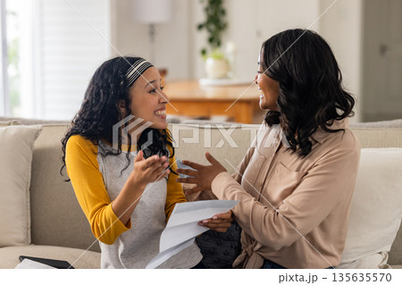 On couch at home, mother and child sharing joyful conversation, discussing documents On couch at home, mother and child sharing joyful conversation, discussing documents 135635570