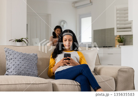 Relaxing at home, woman using smartphone while another works on laptop in background 135635583