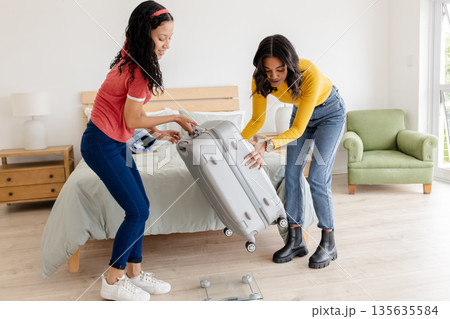 African American women packing suitcase together in bedroom, preparing for travel African American women packing suitcase together in bedroom, preparing for travel 135635584