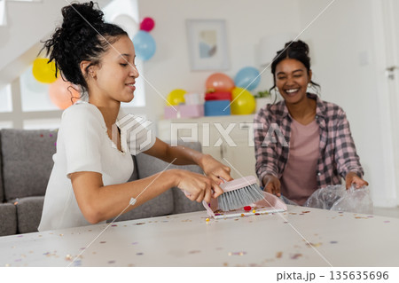 Cleaning up after party, two women sweeping confetti from table, smiling together Cleaning up after party, two women sweeping confetti from table, smiling together 135635696