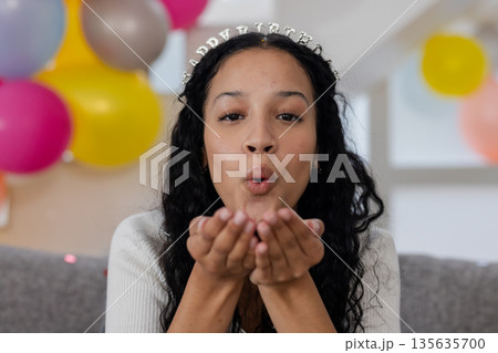Blowing kisses, African American woman celebrating birthday with balloons at home 135635700