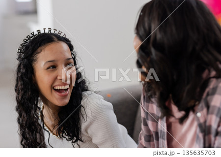 Celebrating birthday, smiling woman wearing tiara talking with friend at home Celebrating birthday, smiling woman wearing tiara talking with friend at home 135635703