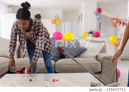 Cleaning up after party, woman tidying living room with balloons and confetti Cleaning up after party, woman tidying living room with balloons and confetti 135635711