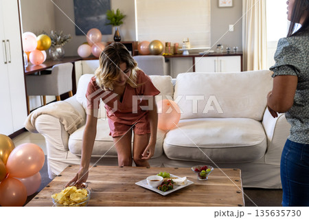 Woman arranging snacks on table in living room, preparing for celebration 135635730