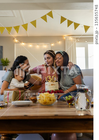 Celebrating at home, diverse women and baby enjoying birthday cake and gifts Celebrating at home, diverse women and baby enjoying birthday cake and gifts 135635748