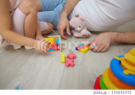 close-up of father and daughter sitting on floor at home, bonding while playing with colorful toys close-up of father and daughter sitting on floor at home, bonding while playing with colorful toys 135635772