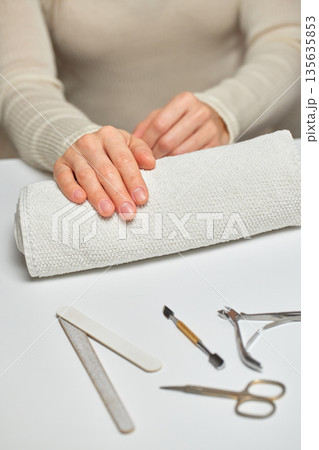 Woman's hands resting on a towel with various manicure tools on a white surface Woman's hands resting on a towel with various manicure tools on a white surface 135635853