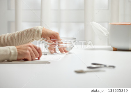 Woman performing hand care, soaking fingers in a glass bowl with water 135635859