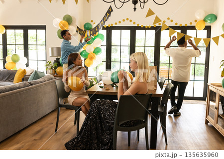 Friends decorating living room with balloons and banners for birthday celebration Friends decorating living room with balloons and banners for birthday celebration 135635960