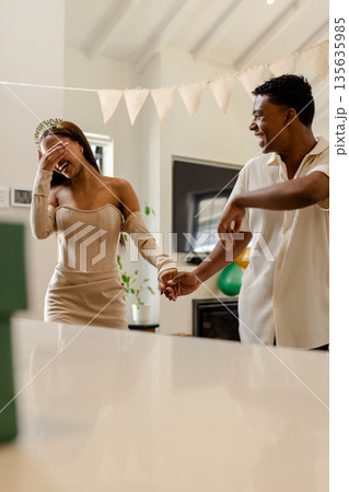 Couple celebrating birthday at home, laughing and holding hands joyfully Couple celebrating birthday at home, laughing and holding hands joyfully 135635985