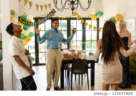 Friends celebrating birthday at home, dancing and laughing with joyful expressions 135635988