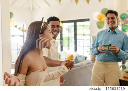 Friends celebrating birthday at home, laughing and exchanging gifts with joy 135635989