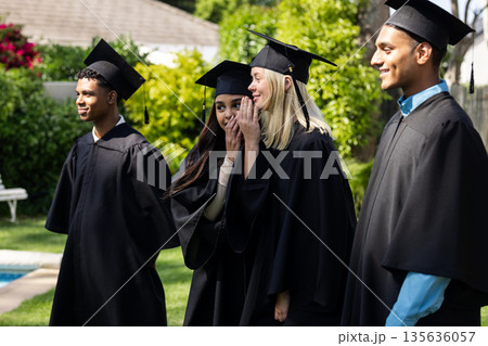 Graduates in caps and gowns celebrating together outdoors, smiling and joyful 135636057