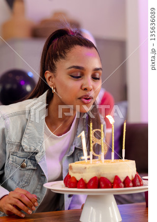 Young woman blowing out candles on birthday cake, celebrating milestone with joy 135636089